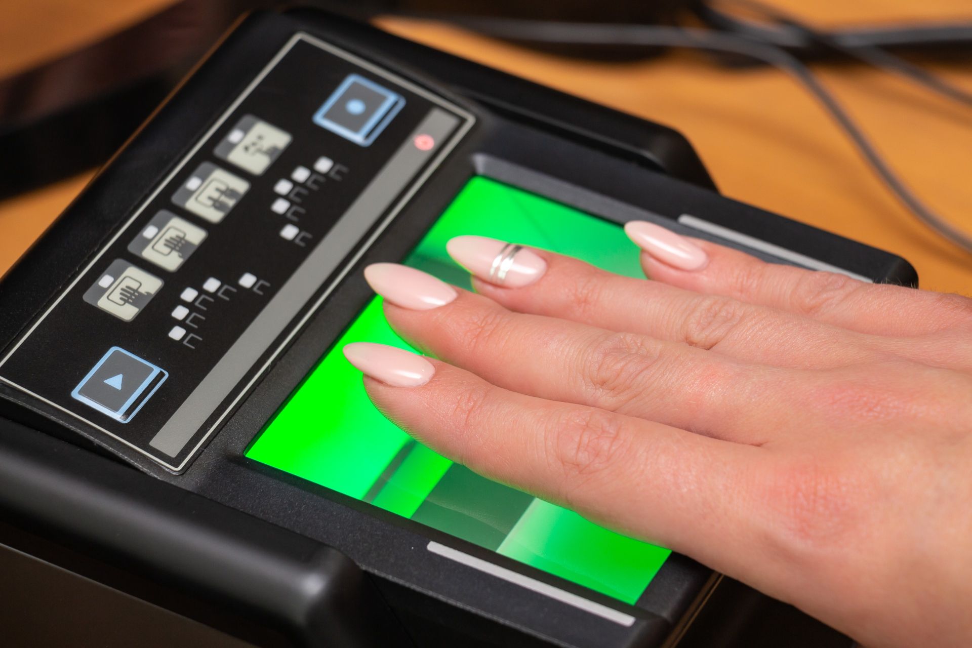Women's hand with fake nails getting finger's scanned on a fingerprinting device.